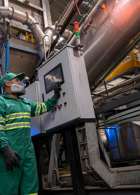 Colaborador de Ciudad Limpia con elementos de protección manipulando un panel de control en una planta industrial de tratamiento.