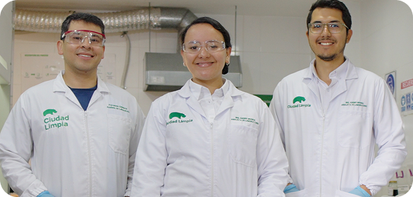 Tres colaboradores de Ciudad Limpia, con batas de laboratorio y gafas de seguridad, posando en un espacio de análisis técnico, reflejando trabajo en equipo y profesionalismo.