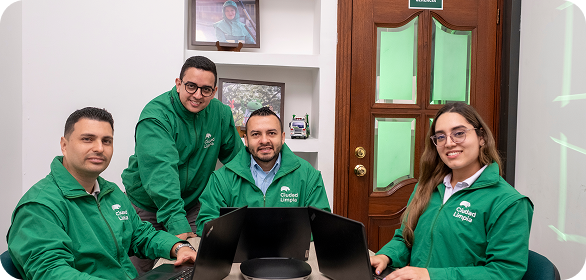 Cuatro colaboradores de Ciudad Limpia posando en una sala de reuniones junto a varios computadores portátiles, en un entorno de trabajo colaborativo y profesional.