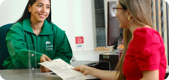 Colaboradora de Ciudad Limpia atiende a una usuaria en un punto de servicio y le entrega un documento, en un ambiente cercano y amable.