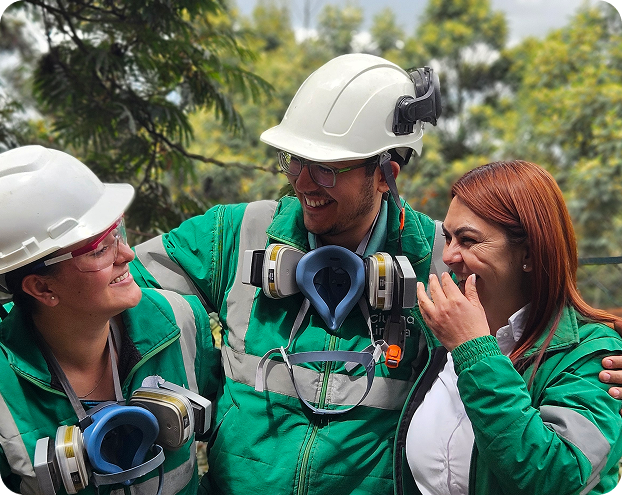 Vista de tres colaboradores de Ciudad Limpia, con cascos y equipos de protección, compartiendo un momento de cercanía y alegría al aire libre durante una jornada de trabajo.