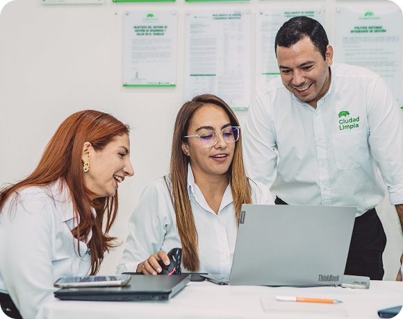 Tres colaboradores de Ciudad Limpia comparten una jornada de trabajo en equipo alrededor de un computador portátil, revisando información en un ambiente colaborativo de oficina.