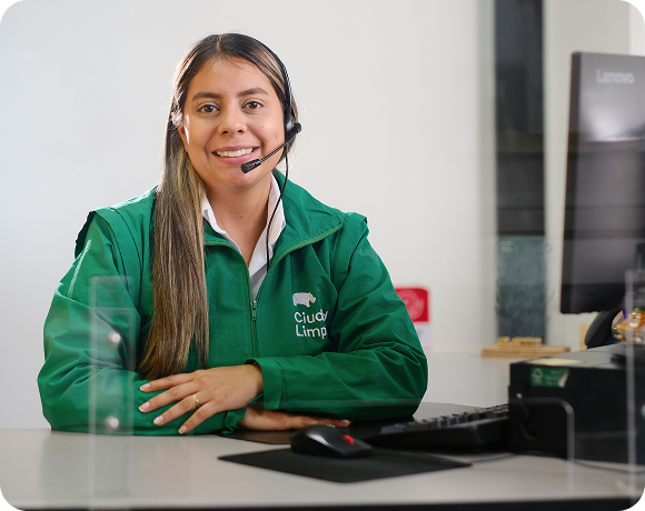 Colaboradora de Ciudad Limpia atendiendo en un punto de servicio con diadema de atención telefónica, sentada frente a un computador y con expresión amable.