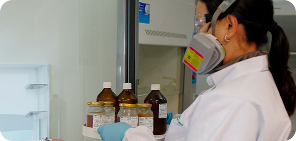 Colaboradora de Ciudad Limpia, con bata de laboratorio, gafas de seguridad, guantes y mascarilla de protección, manipula frascos con muestras en un entorno de análisis técnico.